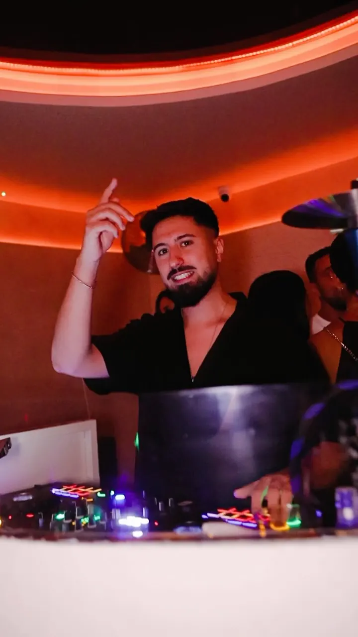 DJ en la cabina iluminada de naranja levantando la mano